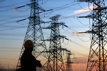 A silhouette of a man in front of a high voltage tower