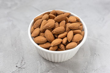 Raw almonds in a porcelain bowl on a gray background