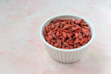 Dried goji berries in a porcelain bowl on a pink background