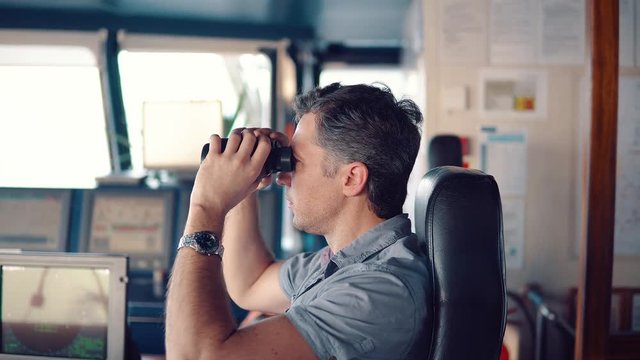 Navigational officer lookout on navigation watch looking through binoculars. Marine industry. COLREG collision regulations