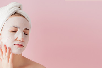 Beautiful young woman is applying a cosmetic tissue mask on a face on a pink background. Healthcare...