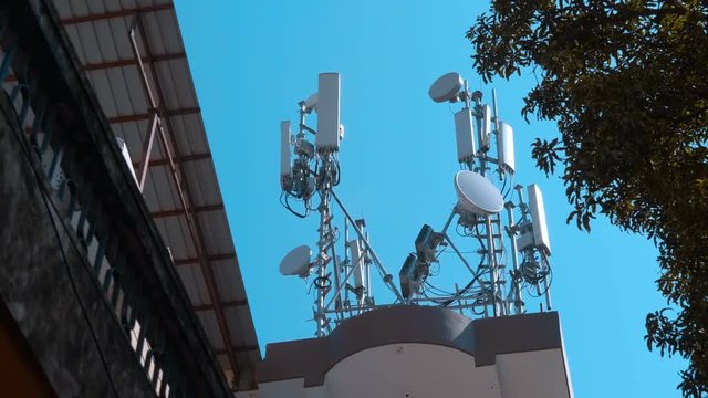 High telecommunication tower standing in Delhi, India. On it are satellite dishes, mobile communication antennas, a radio relay dishes, blocks of the radio module of the base station equipment. Shot i