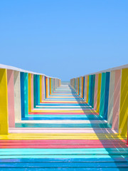 The colorful wood bridge extends into the sea in blue sky