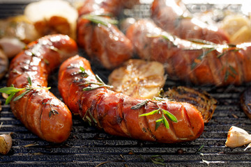 Grilled sausages with the addition of herbs and vegetables on the grill plate, outdoors, close-up....