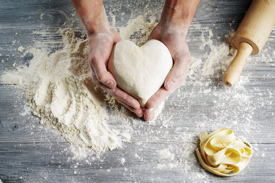 Heart shaped dough held by baker's hands in close-up.