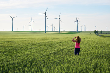 Young woman looking towards wind turbines at sunrise, in a field of green wheat. Concept for sustainable energy solutions in the future. © k5hu