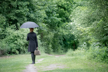 A lonely woman goes with umbrella and travel bag along a forest road. Concept loneliness.