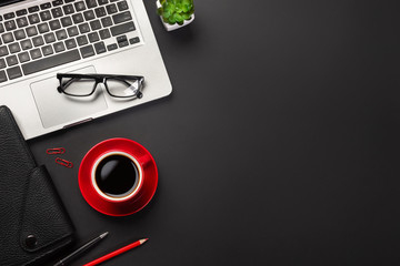 Black office desk table with blank screen laptop computer, notebook, cup of coffee and other office