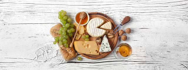 Cheese, honey, grape, nuts and wineglass on cutting board and white wooden table