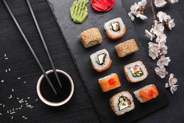 Obraz na płótnie Canvas Set of sushi and maki rolls with branch of white flowers on stone table