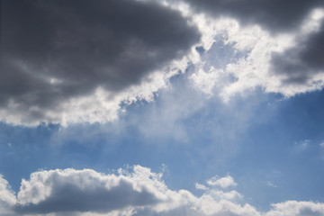 the sun makes the way through dark clouds in the blue sky