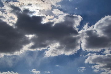 the sun makes the way through dark clouds in the blue sky