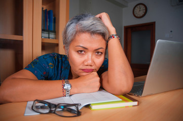 Naklejka na ściany i meble depressed and overworked middle aged attractive Asian woman working in stress on laptop computer desk feeling upset and overwhelmed in upset face expression