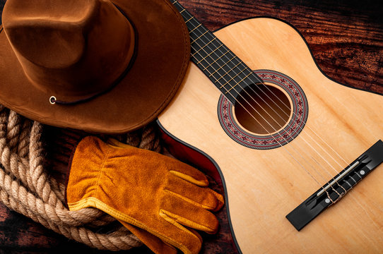 American culture, living on a ranch and country muisc concept theme with a cowboy hat, acoustic guitar, farm gloves and a rope lasso on a wooden background in a old saloon - Powered by Adobe