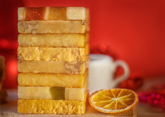 The pyramid of the turron with marmalade on a wooden tray, a red background with Christmas decorations. Cup of coffee. Selective focus. Blurred background. Spanish Christmas candy. Slices of lemon.
