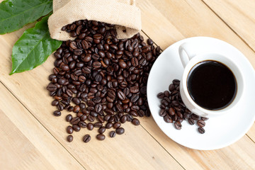 black coffee cup with beans and leaves isolated on wood background, coffee beans in sack