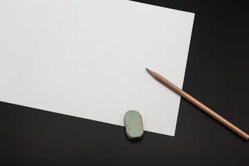 a piece of white paper, a brown pencil and an eraser, placed on the black class desktop