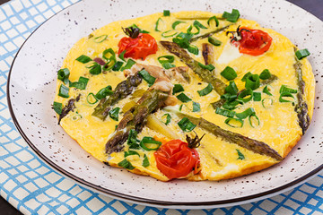 Omelette with asparagus and tomato for breakfast on a wooden background.