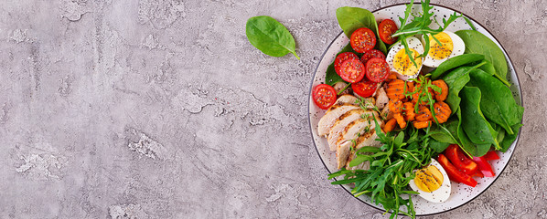 Plate with a keto diet food. Cherry tomatoes, chicken breast, eggs, carrot, salad with arugula  and...