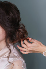 Naklejka premium Hairdresser at work in process of creating wedding hairstyle. Hand hairdresser straightens brown curls. Perfect and beauty in details. Beauty industry