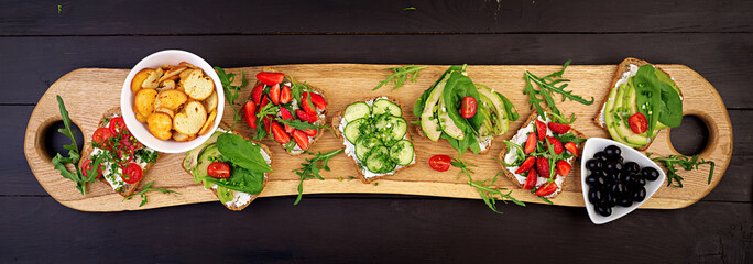 Flat lay of healthy vegetarian dinner table setting. Sandwiches with tomato, cucumber, avocado, strawberry, herbs and olives, snacks. Banner. Clean eating, vegan food
