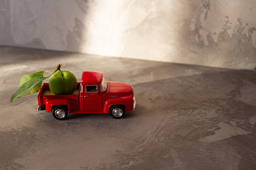 Obraz na płótnie Canvas Green plum on old vintage red toy truck car. Fruits and transportation concept in macro. Close-up food logistics visualisation.