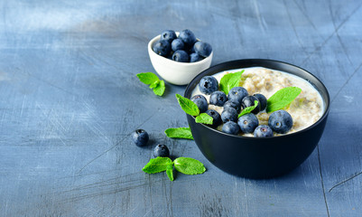 Oatmeal cereal porridge with fresh berries  in black bowl. Healthy breakfast. Top view on gray  table