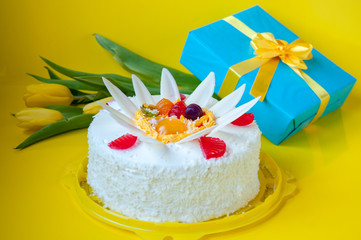 Festive white cake decorated with jelly, tulips and gift on a yellow background