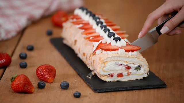 Close up, young girl is cutting meringue roulade with berries and mascarpone.