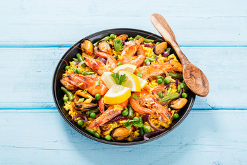 Traditional spanish seafood paella in the fry pan on a blue wooden  table.