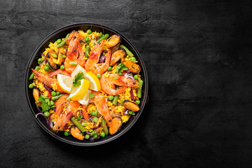 Traditional spanish seafood paella in the fry pan on a black wooden  table, top view.