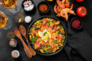 Traditional spanish seafood paella in the fry pan on a black wooden  table, top view.