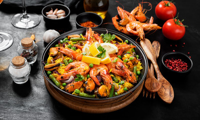Traditional spanish seafood paella in the fry pan on a black wooden  table. - obrazy, fototapety, plakaty