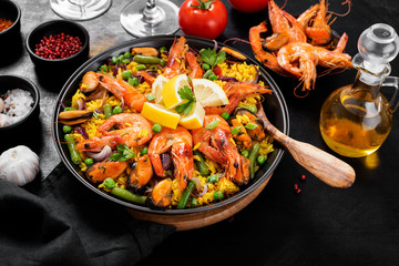 Traditional spanish seafood paella in the fry pan on a black wooden  table.