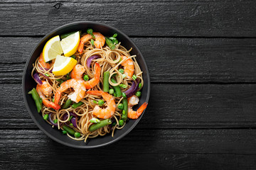 Stir fry noodles with shrimps and vegetables in black bowl.