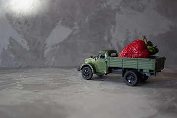 Red strawberry on old vintage green toy truck car. Fruits and transportation concept in macro. Close-up food logistics visualisation.