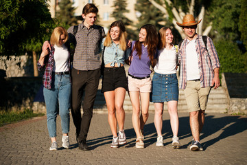 Friendship, togetherness, traveling, vacation, holidays, sightseeing, city tour, student exchange program. Group of young people with backpacks hugging walking in the city