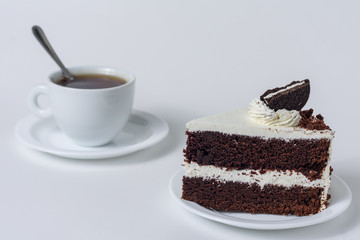 A slice of cake with chocolate chip cookies on a white plate and a mug of tea