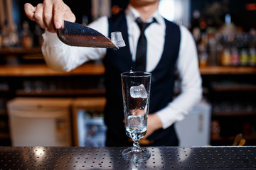 The bartender prepares a fresh, cold, alcoholic cocktail. Bar employee puts ice in his glass