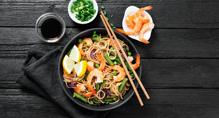 Stir fry noodles with shrimps and vegetables in black bowl.
