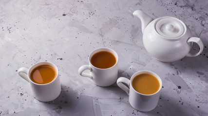 White teapot and white cups of tea or coffee on a gray table