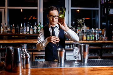 elegant young male barman prepares a delicious cocktail at the bar