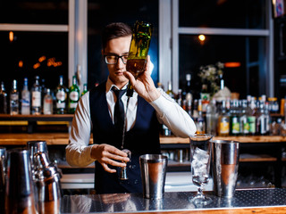 elegant young male barman prepares a delicious cocktail at the bar