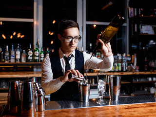 elegant young male barman prepares a delicious cocktail at the bar