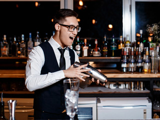 elegant young male barman prepares a delicious cocktail at the bar