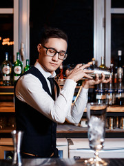 elegant young male barman prepares a delicious cocktail at the bar
