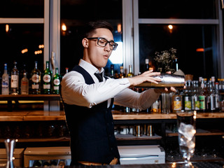 elegant young male barman prepares a delicious cocktail at the bar