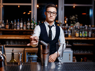 elegant young male barman prepares a delicious cocktail at the bar