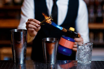 elegant young male bartender preparing a delicious cocktail at the bar. barman szmat razmarin gas torch