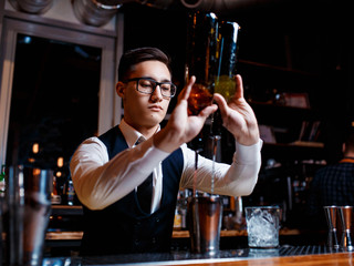elegant young male barman prepares a delicious cocktail at the bar